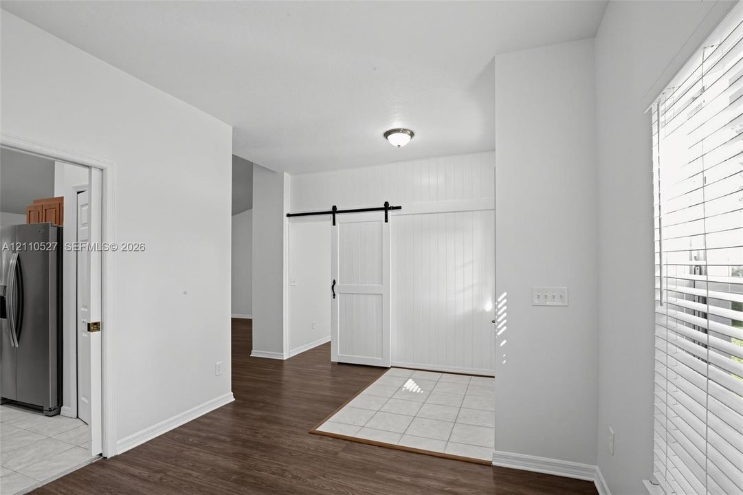 Interior featuring wood-finish flooring, white vertical-plank wall detailing, and a black metal sliding barn door