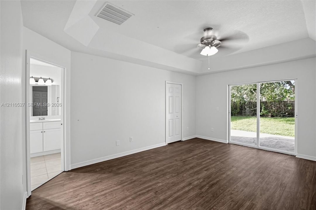 Room featuring wood-finish flooring, tray ceiling with a central ceiling fan, and sliding glass doors with exterior patio access