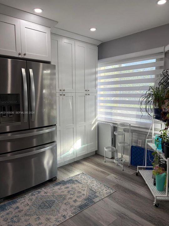 Shaker-style white cabinetry, floor-to-ceiling built-in pantry storage, stainless steel refrigerator, and wood-finish flooring