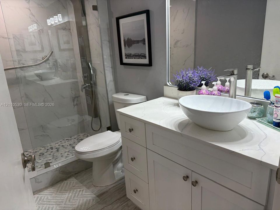 Bathroom featuring a vanity with a white vessel sink, quartz countertop, walk-in shower with stone-tile flooring, floor-to-ceiling tile surround, and polished hardware