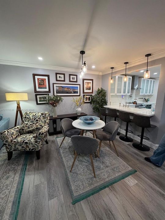 Open-concept kitchen area featuring a stone-topped breakfast bar, recessed ceiling lighting, glass-paneled cabinetry, wood-finish flooring, and crown molding