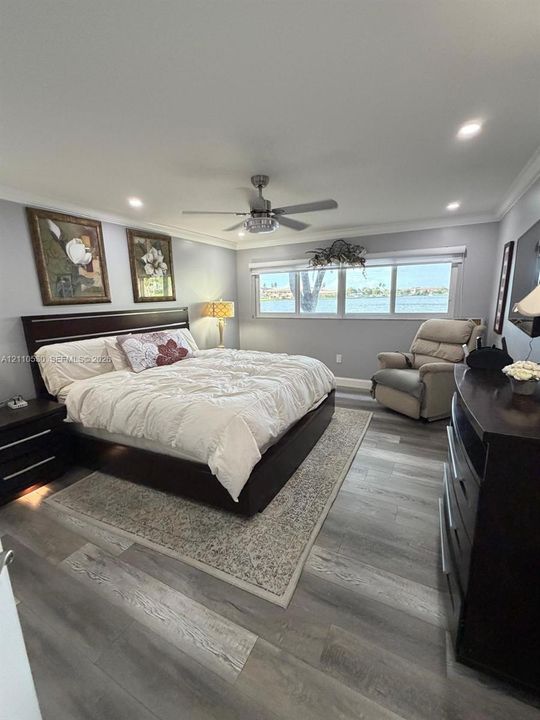 Wood-finish flooring, recessed ceiling lighting, a multi-blade ceiling fan, and large windows with water scenery