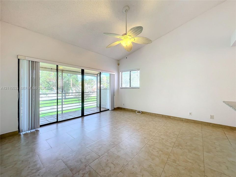 Vaulted ceiling with an integrated multi-blade ceiling fan, large sliding glass doors, neutral tile flooring, and oversized windows