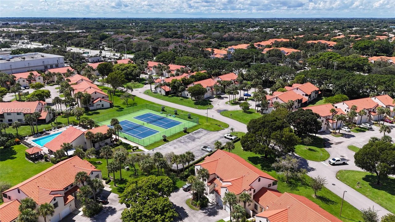 Aerial perspective featuring a community tennis court, a swimming pool, and tiled-roof residential structures set within landscaped grounds