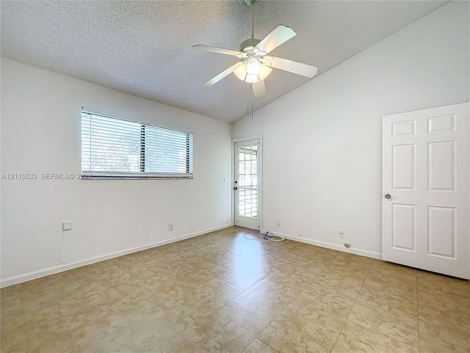 Vaulted ceilings, large-format neutral tile flooring, white-finished six-panel door, glass-paneled exterior door, and integrated ceiling fan with light fixture