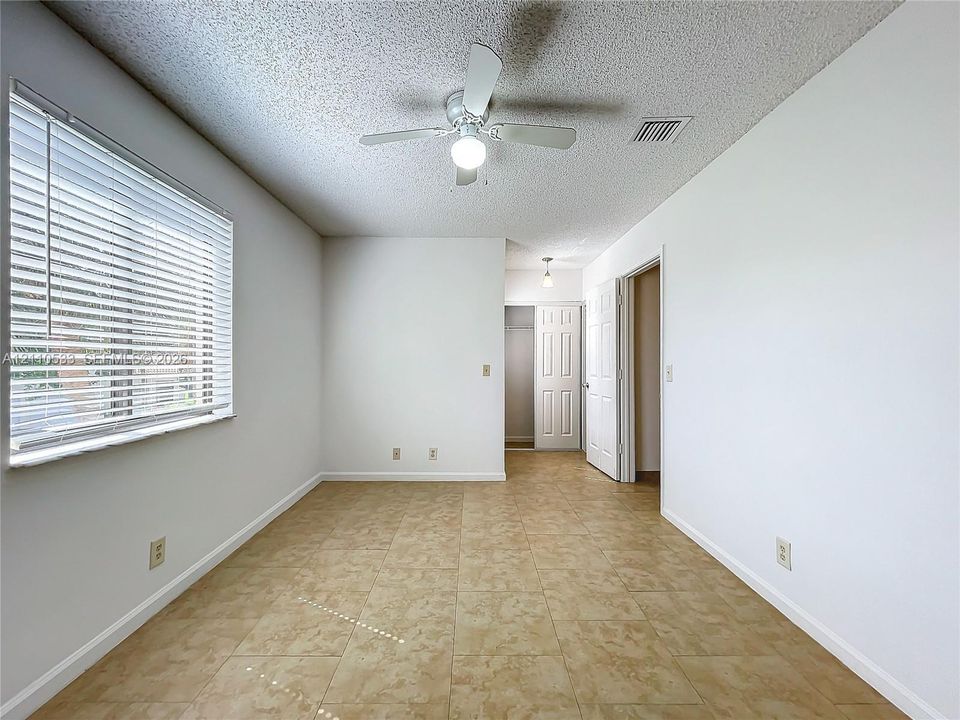Neutral-toned interior space featuring ceramic tile flooring, a ceiling fan with integrated lighting, and horizontal window blinds