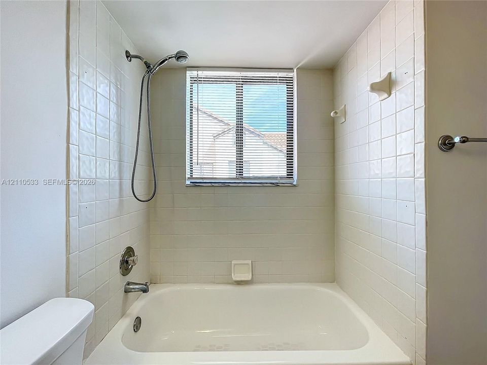 Tub and shower combination featuring a white porcelain finish, square wall tiling, a chrome handheld shower fixture, and a built-in recessed soap dish