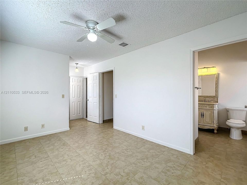 Interior space featuring neutral-toned tile flooring, a white ceiling fan with integrated lighting, and white paneled doors
