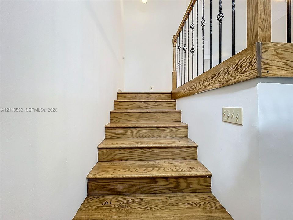 Staircase featuring wood-finish treads, a wood handrail, and black metal balusters