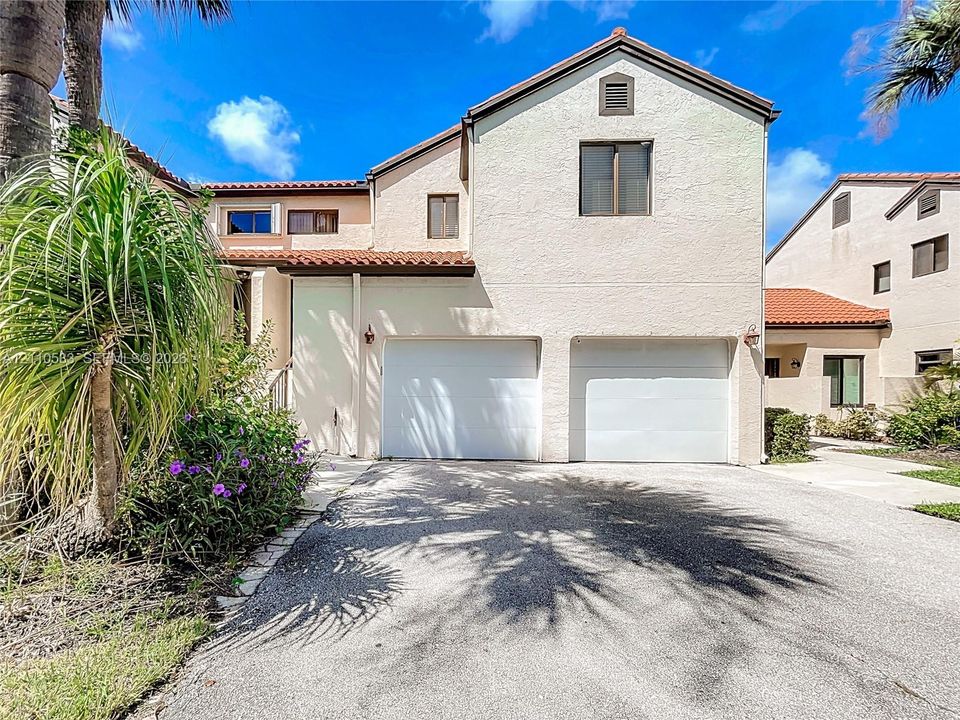 Stucco exterior featuring a two-car garage, pitched tile roof, and low-maintenance landscaping