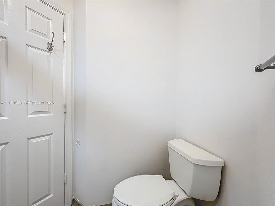 White porcelain toilet, paneled interior door with metal hook, and wall-mounted metal hardware