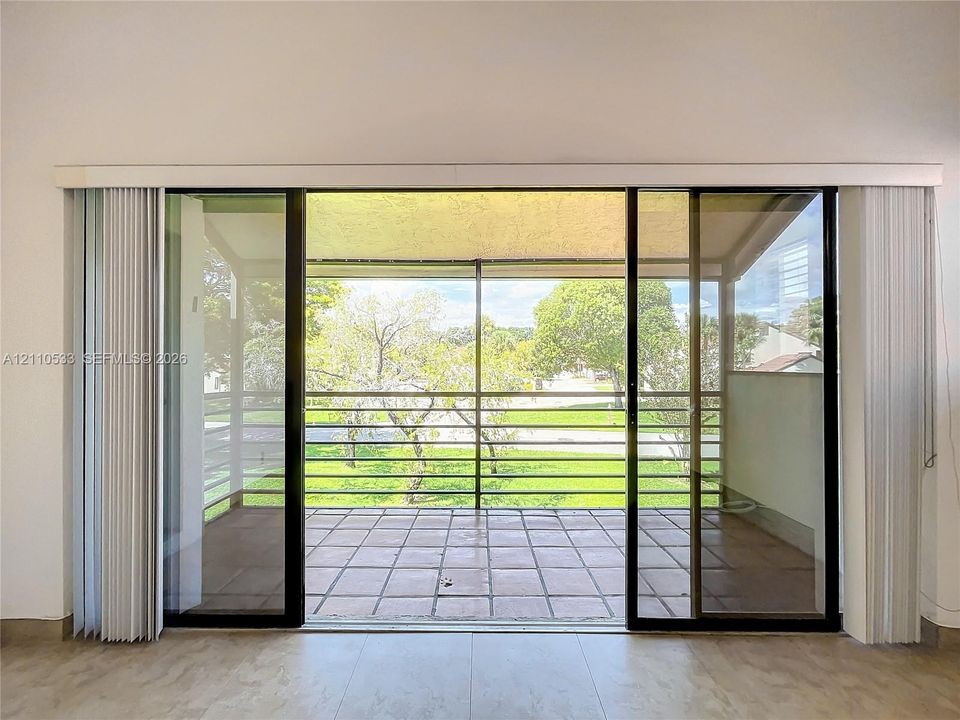 Large sliding glass doors opening to a covered patio with tile flooring, horizontal metal railings, and screen enclosure