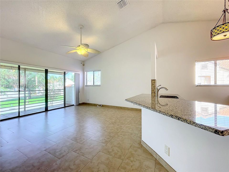Vaulted ceilings, stone-surface breakfast bar with integrated faucet, large-format tile flooring, ceiling fan, and floor-to-ceiling sliding glass doors