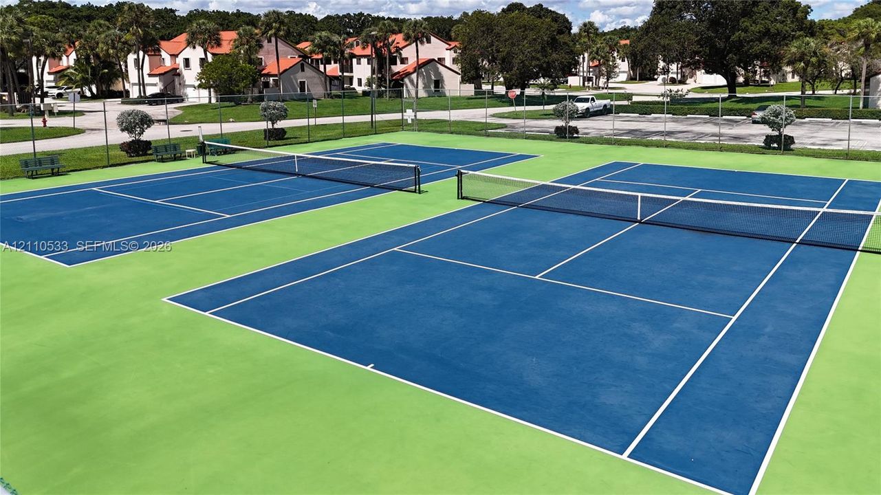 Dual outdoor tennis courts featuring color-contrasted hard surfaces and perimeter chain-link fencing