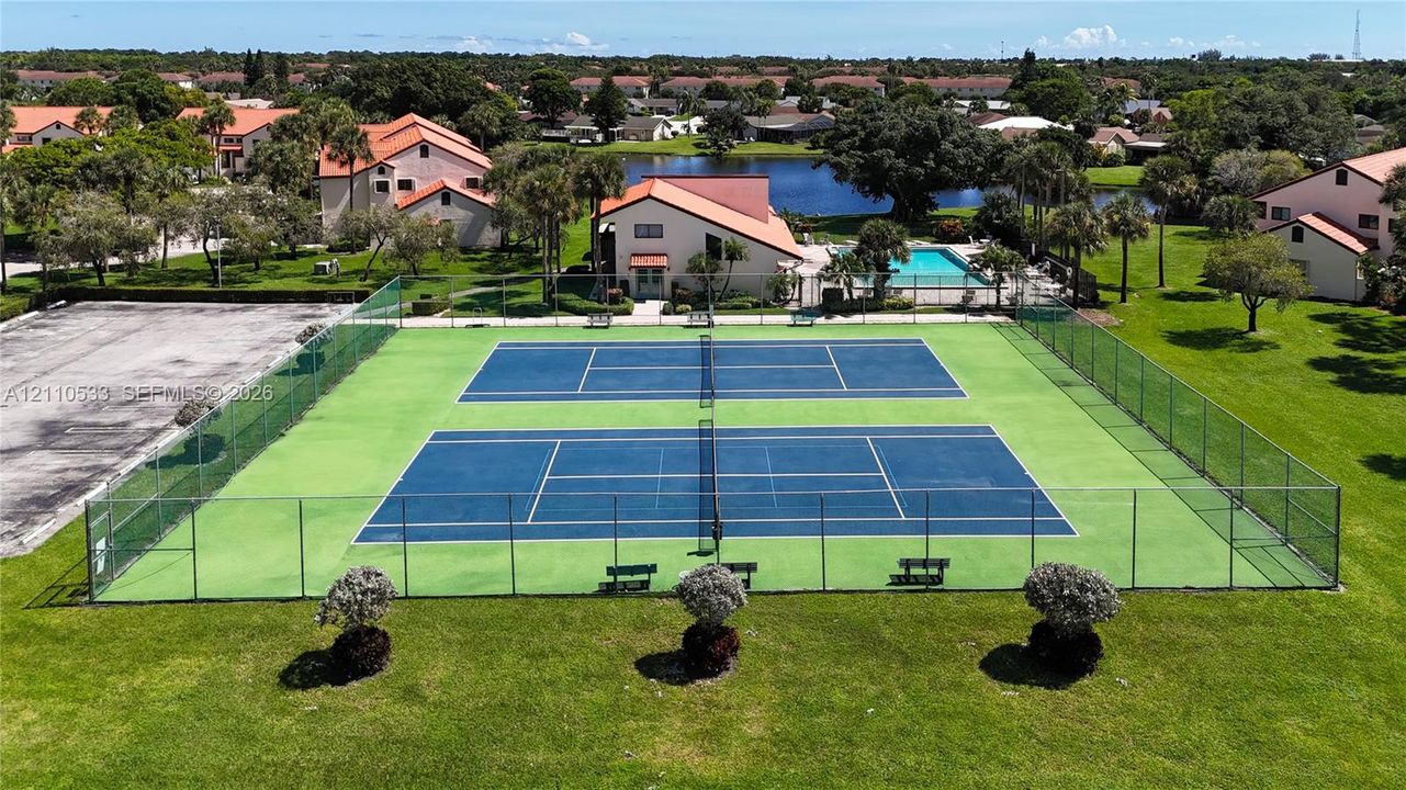 Dual hard-surface tennis courts featuring perimeter chain-link fencing and built-in benches