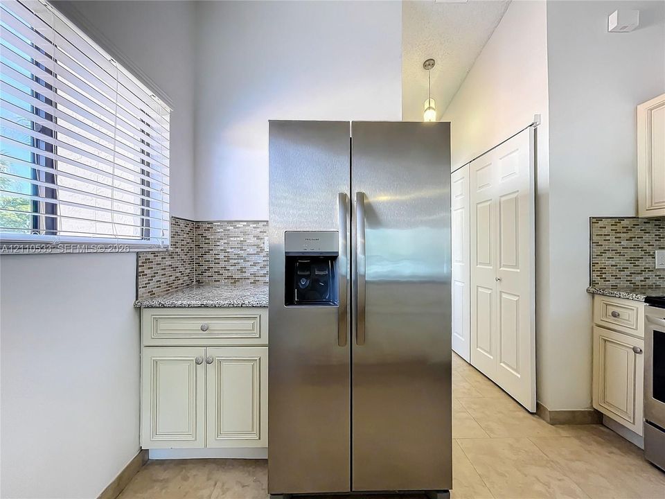 Stainless steel side-by-side refrigerator, multi-toned mosaic tile backsplash, stone-finish countertops, shaker-style cabinetry, and porcelain tile flooring