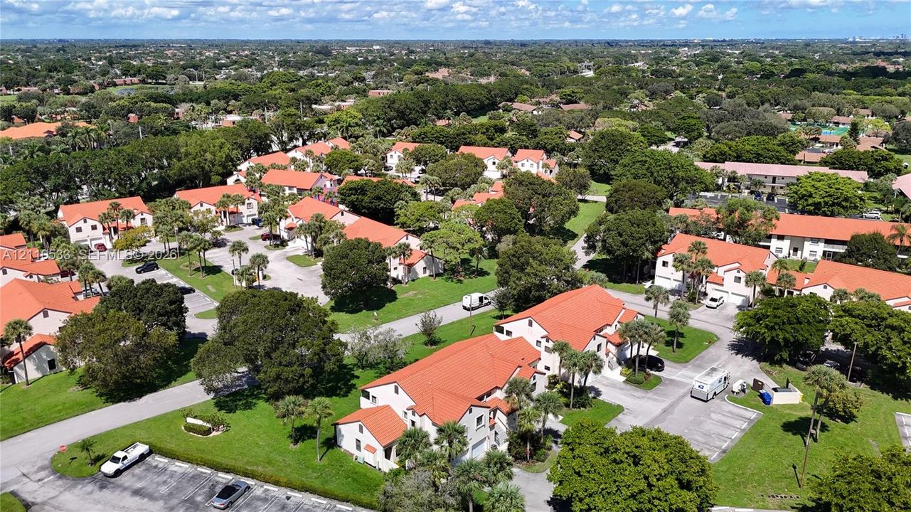 Aerial perspective of a multi-unit residential community featuring clay tile roof systems, stucco exteriors, mature trees, and paved parking surfaces