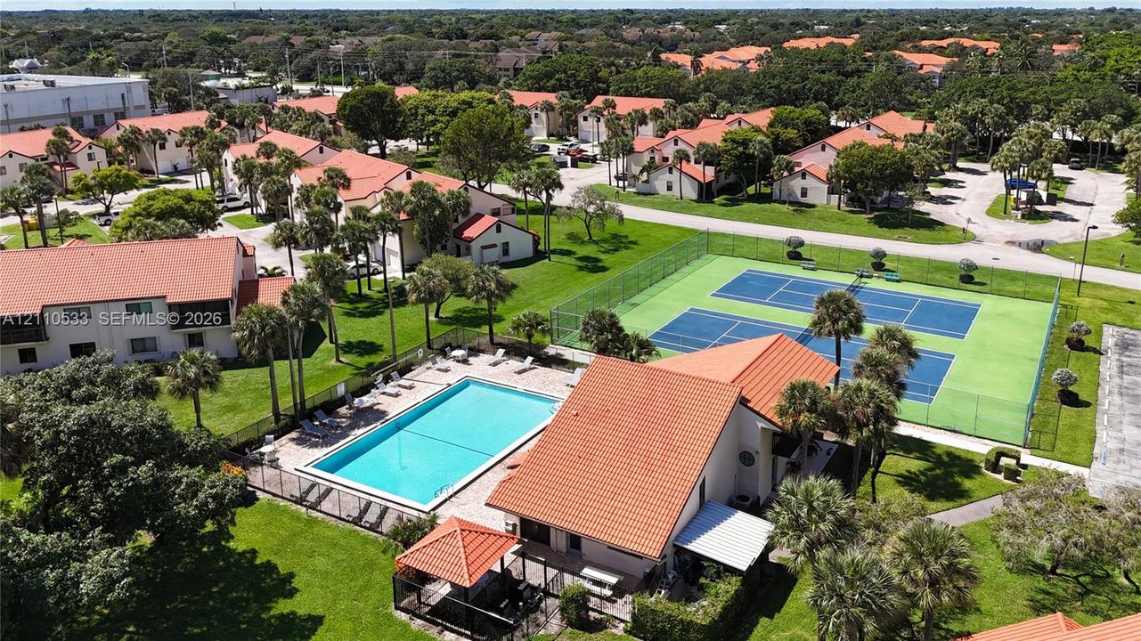 Community amenities featuring a swimming pool with deck, two hard-court tennis courts, and a covered gazebo structure, situated within landscaped grounds with mature palm trees