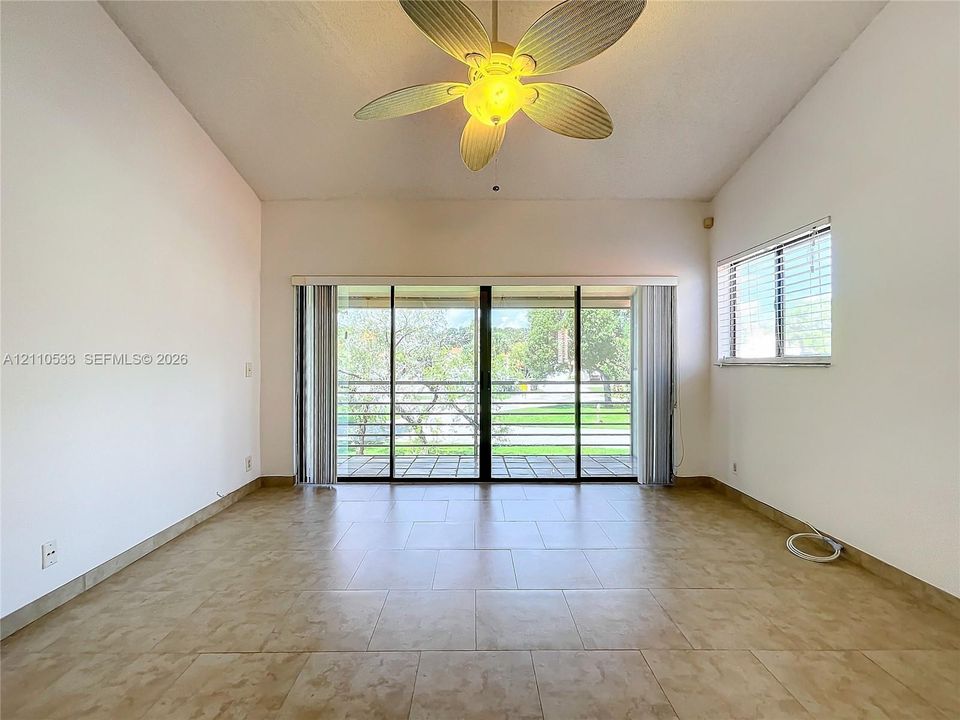 Vaulted ceiling with a central multi-blade ceiling fan, large-format tile flooring, and expansive glass sliding doors