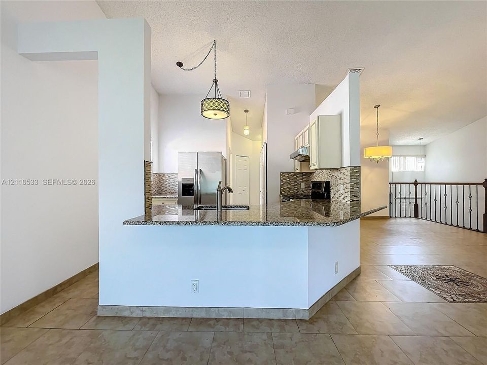 Kitchen featuring stone countertops, tile backsplash, stainless steel refrigerator, patterned pendant lighting, and ceramic tile flooring