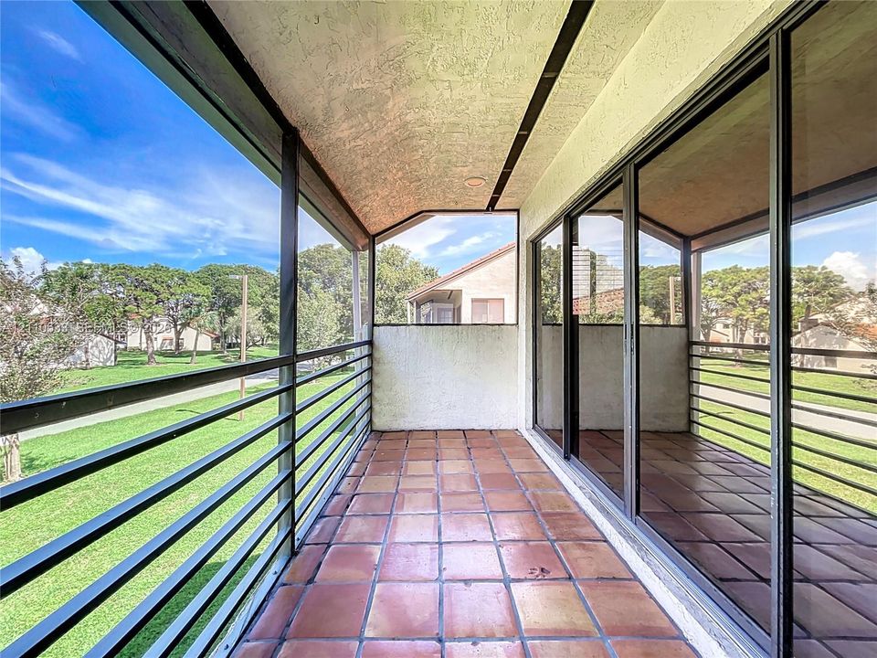 Screened-in balcony featuring terra-cotta tile flooring, black metal railing, and sliding glass doors