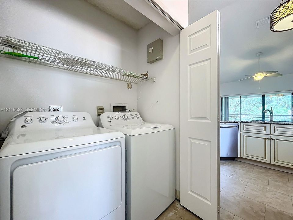 Laundry area featuring a wire-grid shelving unit and a white paneled door, with stone-finish tile flooring and cabinetry visible in the background
