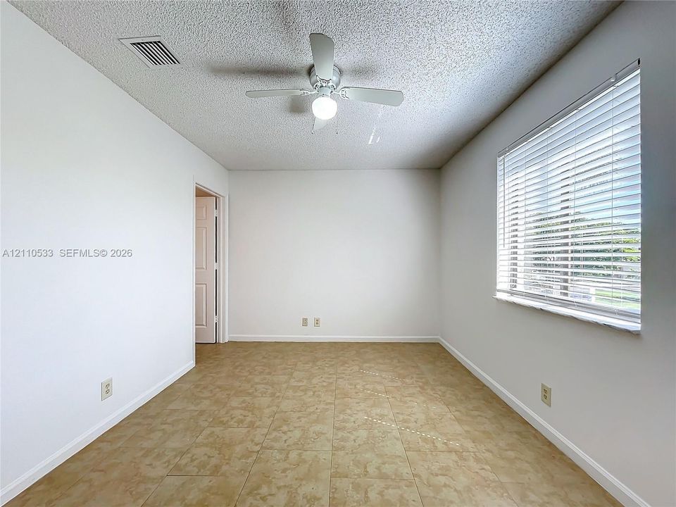 Neutral-toned wall finish, large-format tile flooring, multi-blade ceiling fan with integrated lighting, and horizontal window blinds
