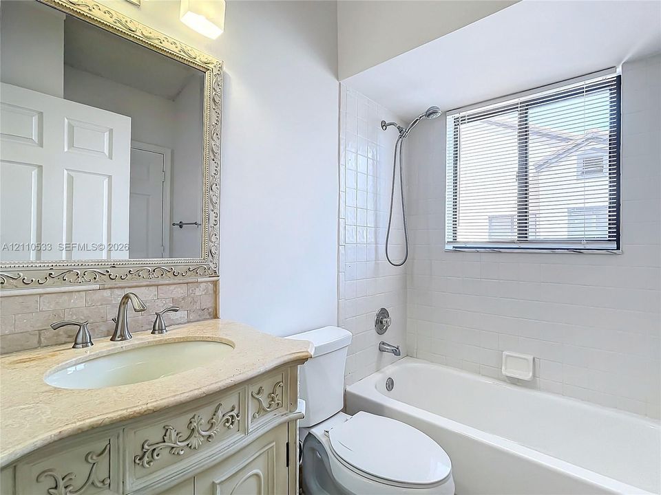 Vanity with decorative millwork, stone-finish countertop, undermount sink, wall-mounted framed mirror, and tiled shower-tub combination