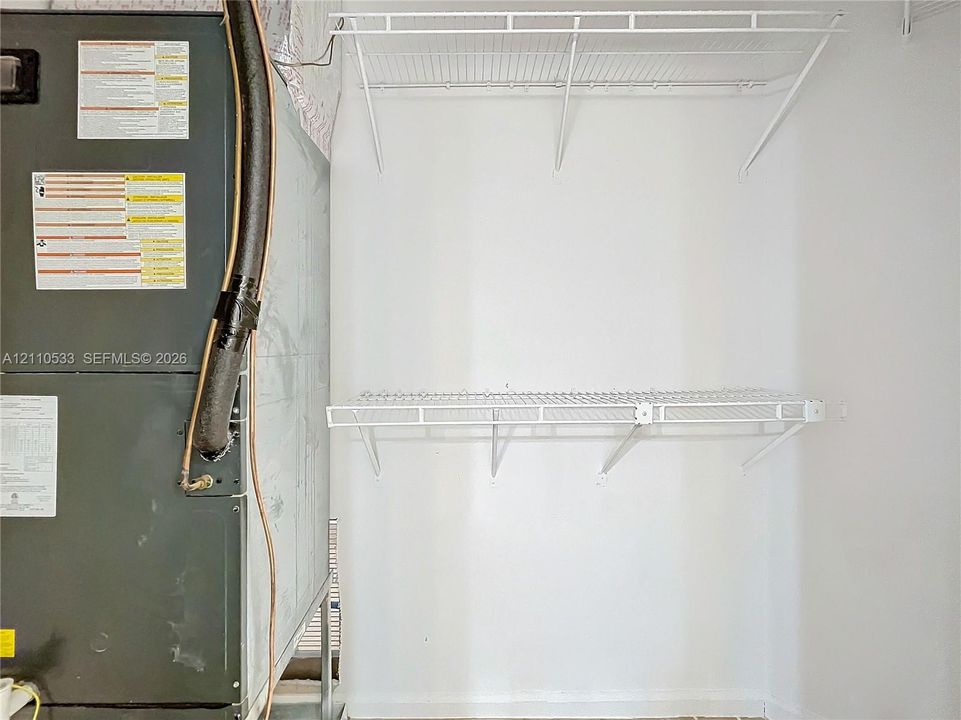 Utility closet featuring an HVAC system and two levels of wall-mounted wire shelving
