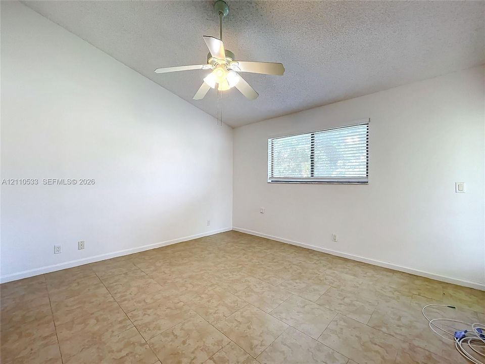 Vaulted ceilings featuring a central ceiling fan with integrated lighting, finished with neutral wall paint and tile flooring