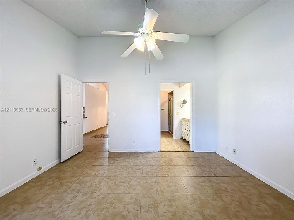 High-ceiling room featuring large-format tile flooring, a multi-blade ceiling fan with integrated light fixture, and two interior doorways