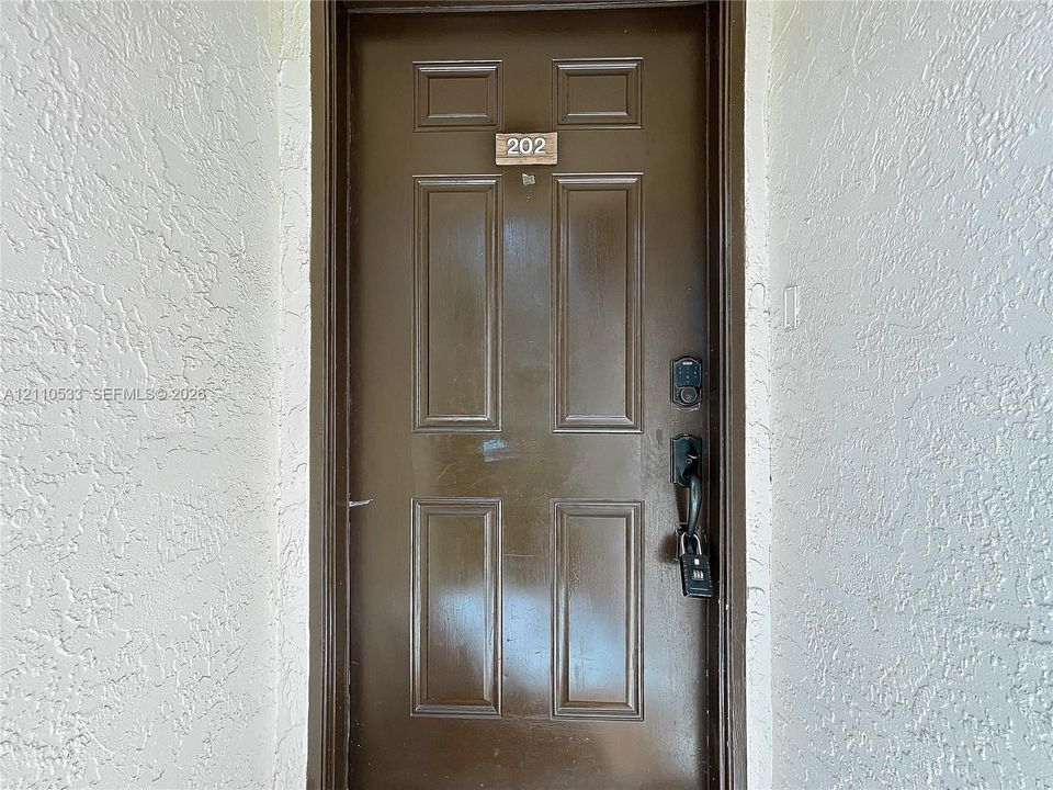Brown six-panel entry door featuring a matte black handle set, electronic keypad lock, and unit numbering
