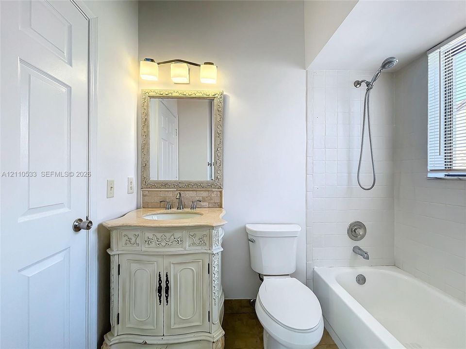Bathroom featuring an ornate vanity with a stone countertop, an integrated sink, a framed wall mirror, three-light fixture, and a tiled bathtub surround with a handheld shower head