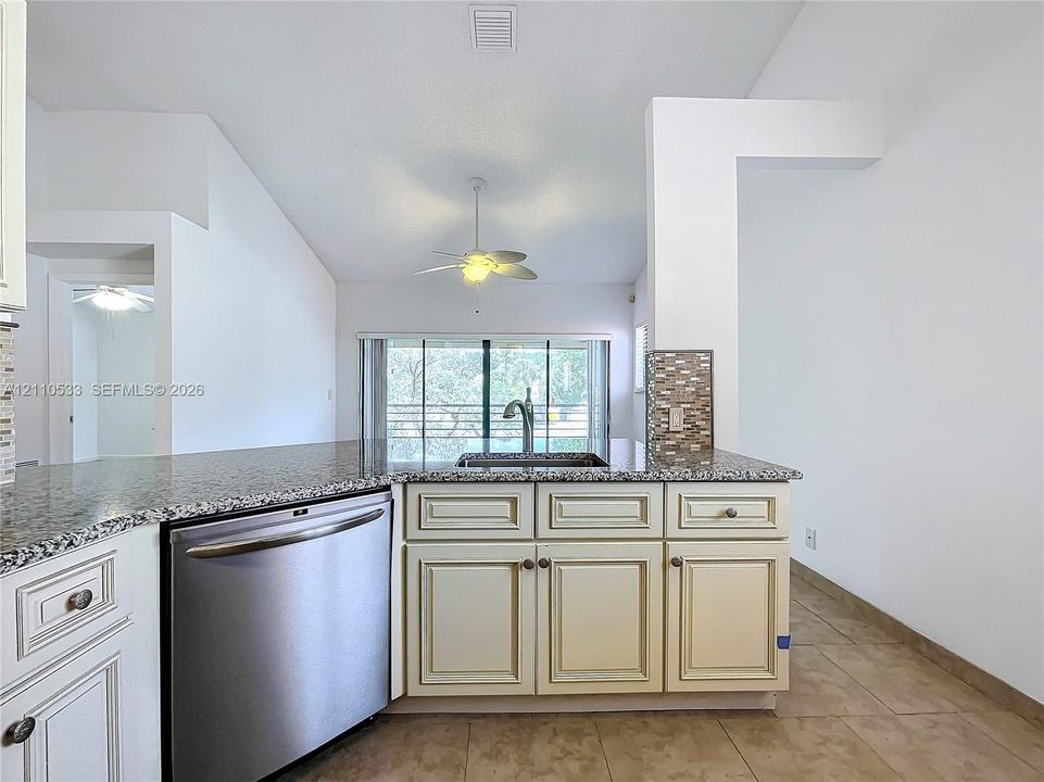 Kitchen featuring a stone-topped peninsula, stainless steel dishwasher, tile backsplash, vaulted ceiling, and recessed ceiling fan