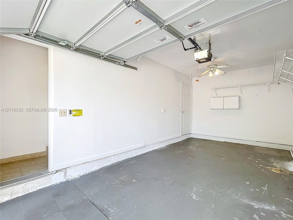Garage interior featuring an automated overhead door system, ceiling-mounted lighting with an integrated fan, built-in wall shelving, and a painted concrete floor