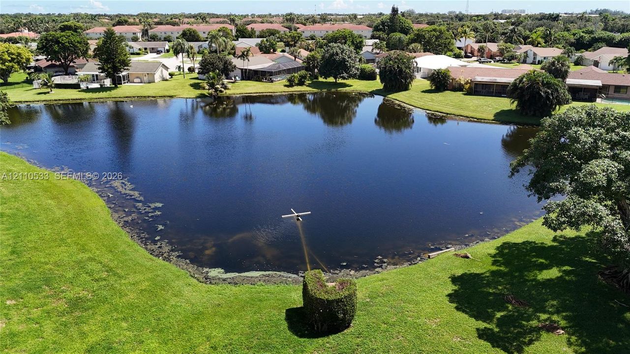 Aerial perspective of a pond surrounded by manicured lawns, mature trees, and residential landscaping