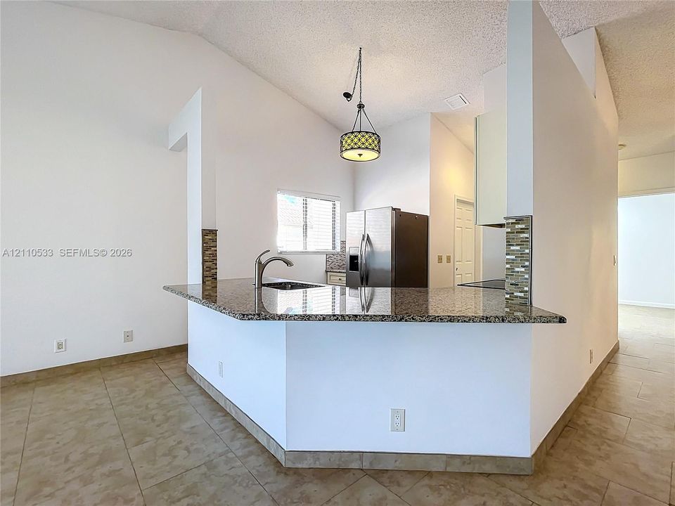 Kitchen featuring a peninsula with stone-finish countertops, stainless steel sink, decorative glass tile accents, stainless steel refrigerator, and a drum-style pendant light