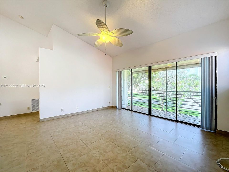 Vaulted ceiling featuring a central lighted paddle ceiling fan, ceramic tile flooring, and large sliding glass doors opening to a covered balcony with exterior railing