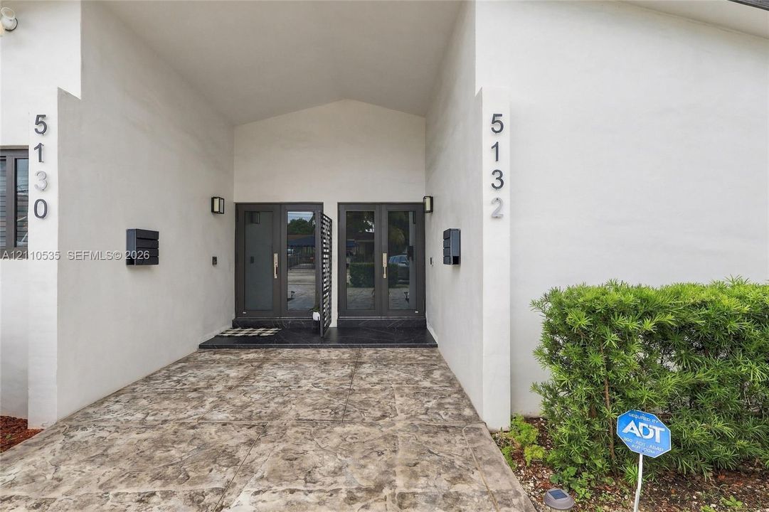 Stucco exterior featuring a covered entryway, dual glass-paneled double doors, and stamped concrete flooring