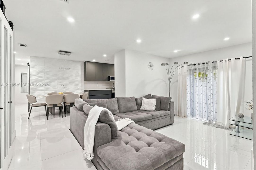 Open-concept interior featuring large-format tile flooring, recessed lighting, a textured accent wall, and cabinetry with a matte finish