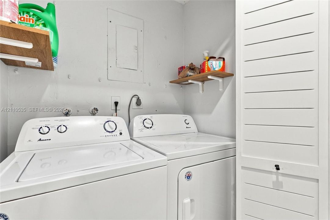 Laundry space featuring wall-mounted wood-finish shelving and a white louvered door cabinet