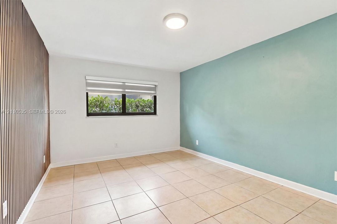 Interior space featuring large-format tile flooring, a decorative wood-slat accent wall, an accent wall painted in a soft blue tone, and a horizontal window with a fitted roller shade