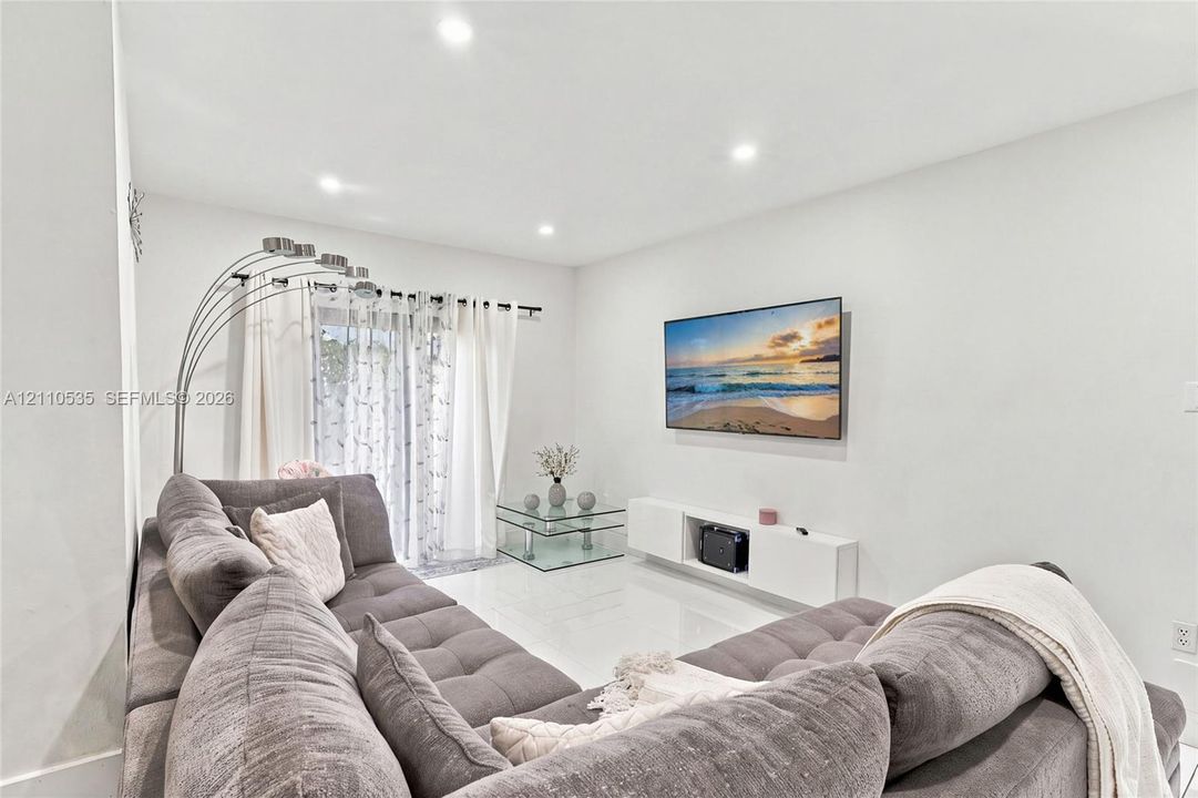 Recessed ceiling lighting, glossy tile flooring, wall-mounted floating media console, and sliding glass door with integrated curtain rod