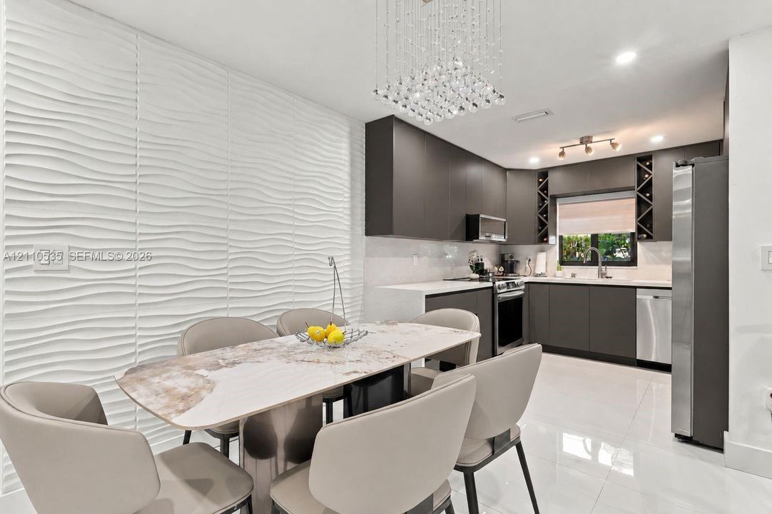 Textured dimensional wall paneling, flat-panel cabinetry, stainless steel appliances, light-toned tile flooring, and a crystal chandelier