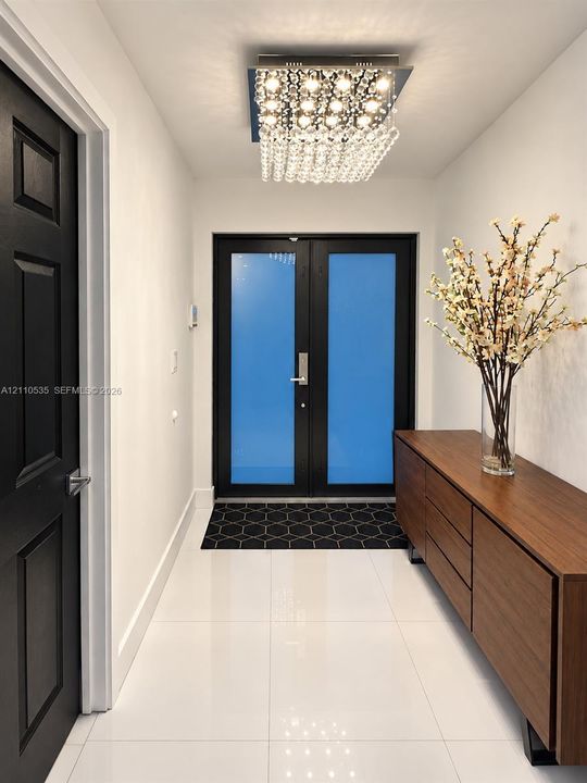 Double entry doors with frosted glass panels, polished tile flooring, black multi-panel door, and a geometric-patterned flush-mount crystal light fixture