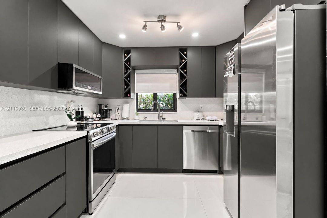 Kitchen featuring matte charcoal flat-panel cabinetry, light-toned stone-finish countertops, stainless steel appliances, built-in wine storage, and polished tile flooring
