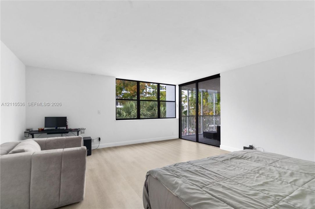 Interior space featuring wood-finish flooring, white walls, multi-pane black-framed windows, and a sliding glass door opening to a railed balcony