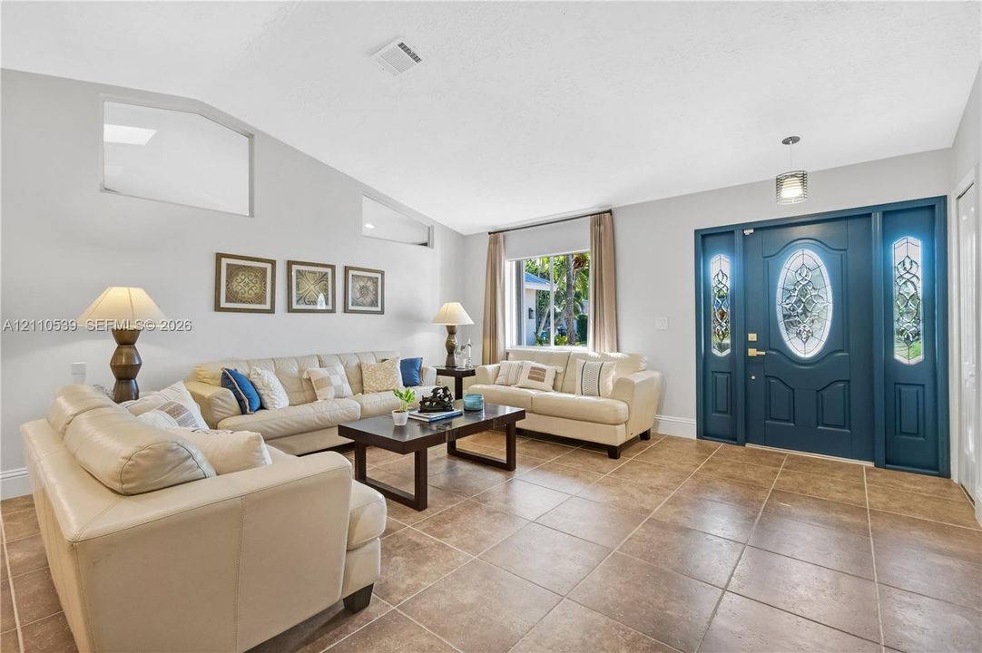 Vaulted ceilings, large-format tile flooring, transom windows, and a decorative front door featuring dual glass-paneled sidelights