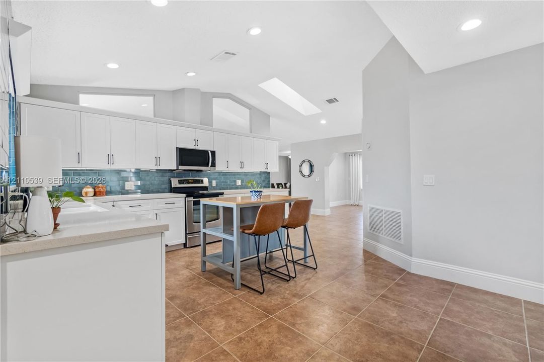 Kitchen featuring white cabinetry, stainless steel appliances, blue tile backsplash, a central island, and a skylight