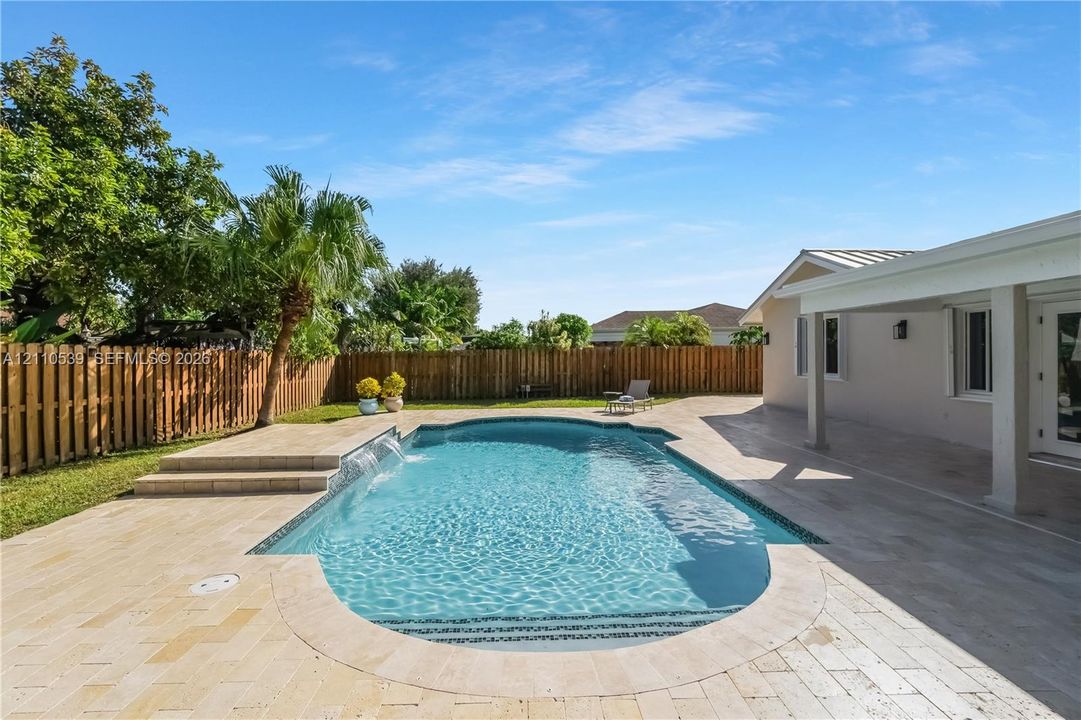 Outdoor swimming pool with built-in water feature, natural stone decking, covered patio, and wood privacy fencing